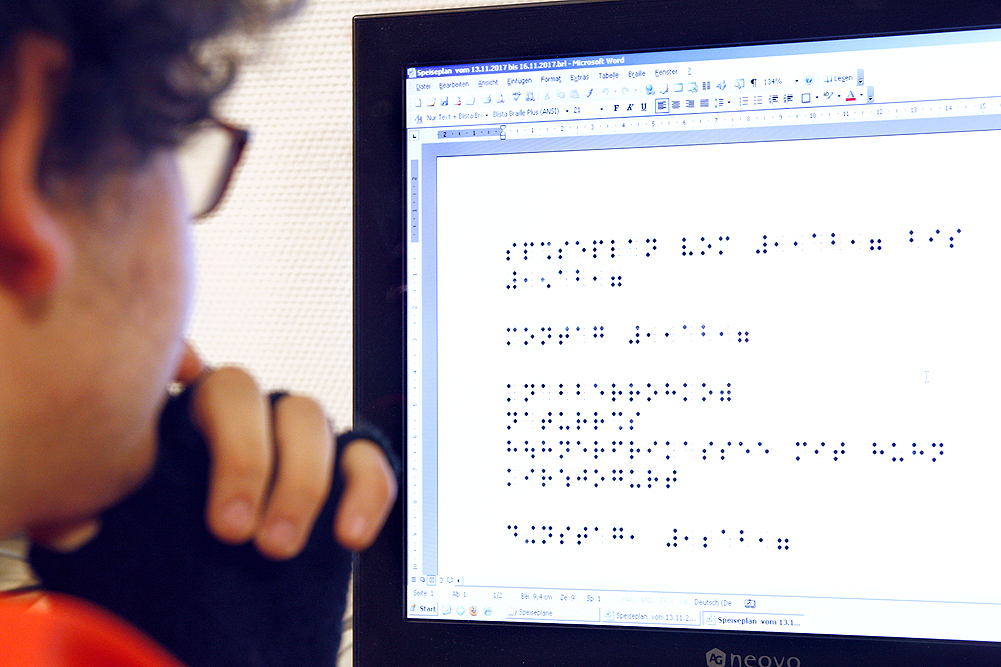 Ein Schüler sitzt vor einem PC-Monitor und sieht sich einen Punktschrifttext an.